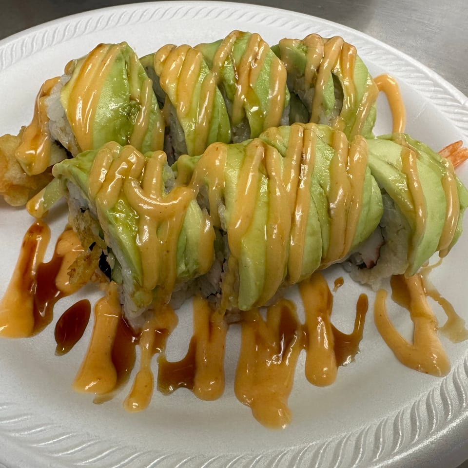 Sushi rolls topped with avocado and drizzled with creamy orange and dark sauces on a white plate.