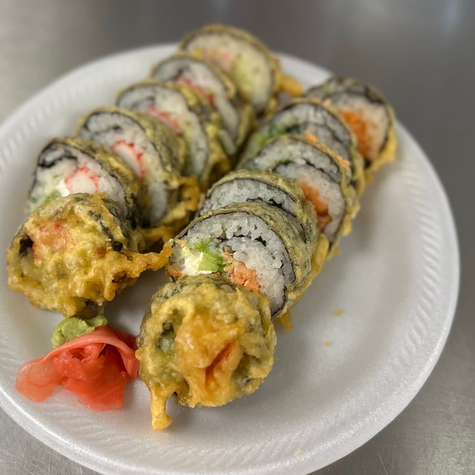 Plate of assorted sushi rolls, including tempura-battered pieces, avocado, seafood fillings, pickled ginger, and wasabi.