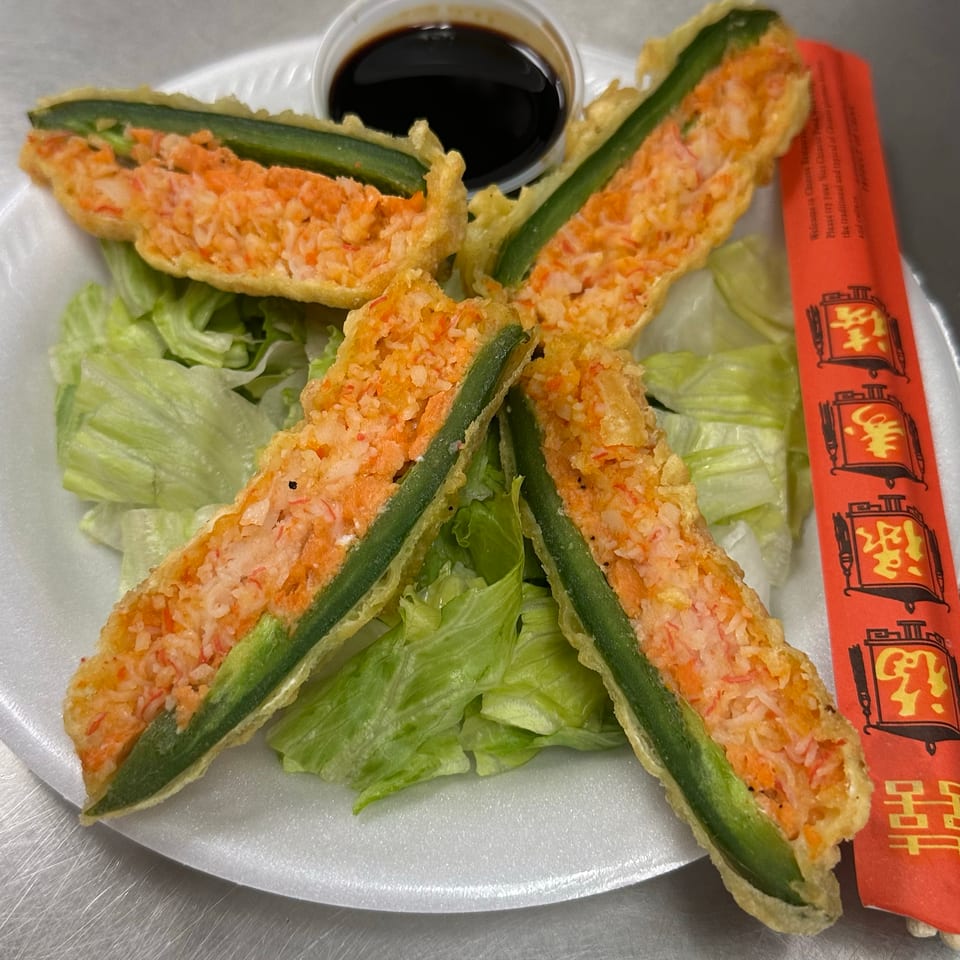 Crispy shrimp-stuffed green pepper halves arranged over lettuce with dark dipping sauce and red chopstick sleeve.