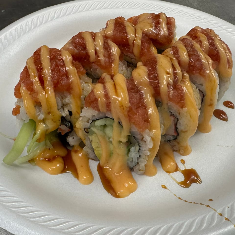 Sushi roll topped with diced salmon and drizzled with creamy orange sauce on a white plate.